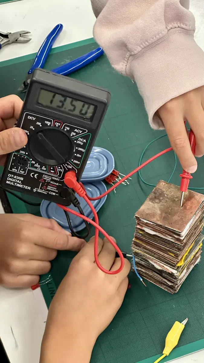 Ein Kind misst mit dem Multimeter die Spannung einer selbst gebauten Batterie
