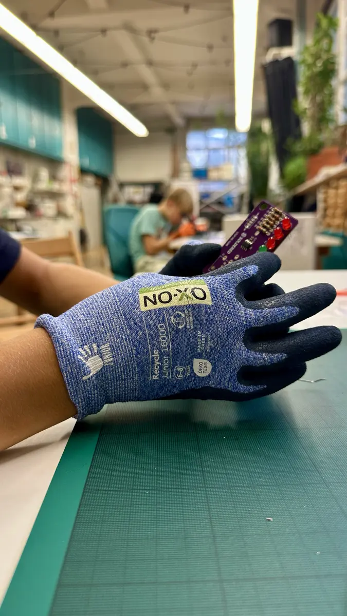 Eine Hand im Arbeitshandschuh hält eine kleine Platine